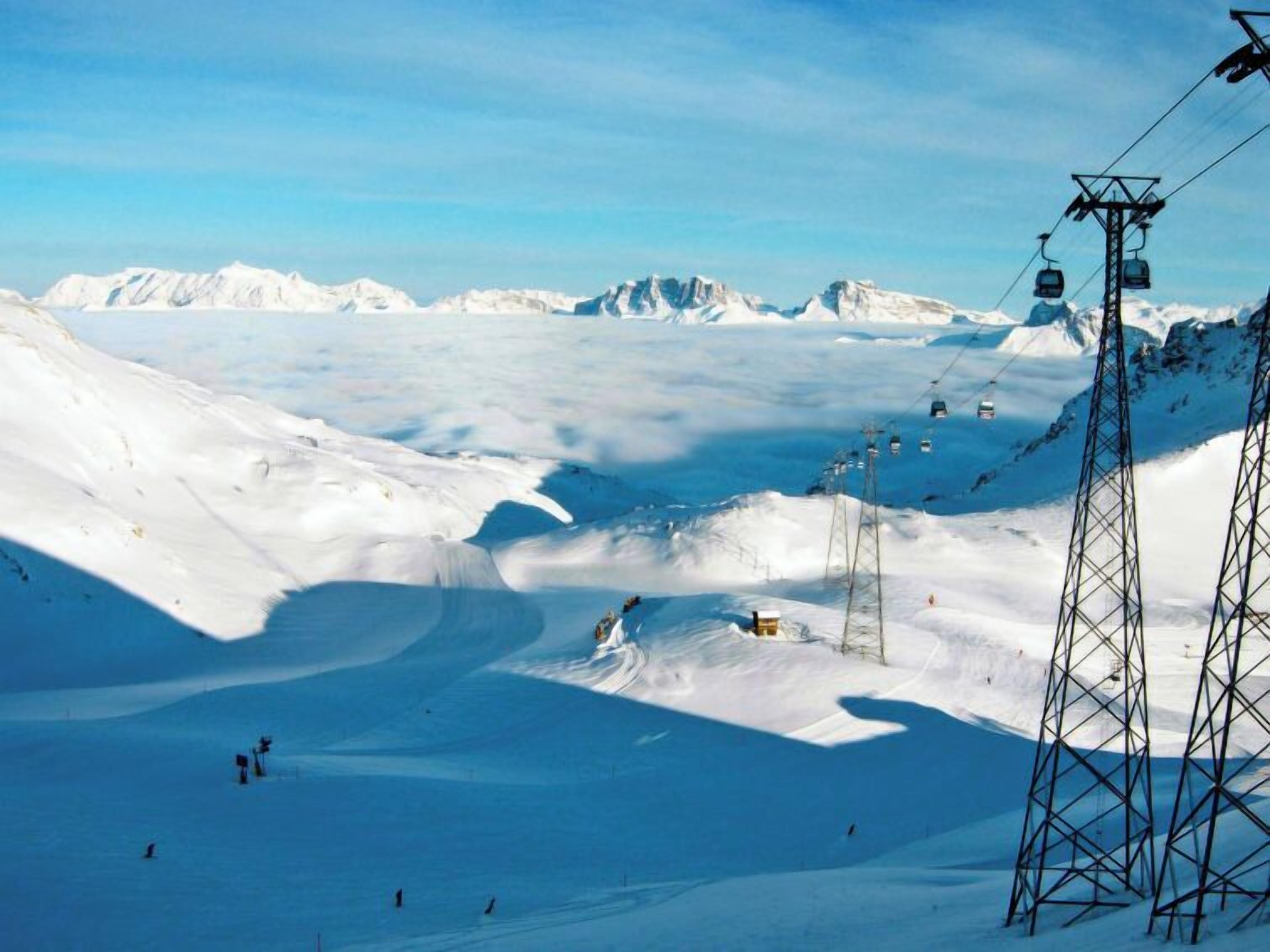 Un paysage de montagne enneigé, avec des remontées mécaniques et un ciel dégagé.