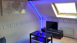 Un petit salon moderne, doté d’un canapé, d’une table basse, d’un téléviseur et d’une lucarne.