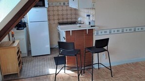 Une cuisine compacte équipée d’un réfrigérateur, d’un four à micro-ondes et d’un petit évier. On y trouve deux chaises noires et un meuble en bois.