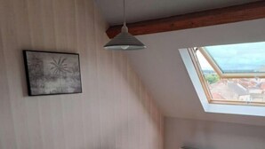 Une chambre à coucher avec un lit, une lucarne, un radiateur et un tableau encadré au mur.