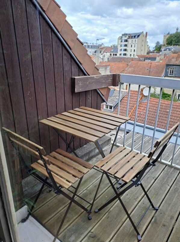 A balcony with a wooden table and chairs, overlooking a cityscape with buildings and a clear sky. - L ' Omerta (Montluçon)