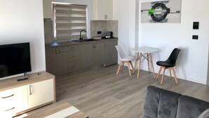 Un salon moderne doté d’un téléviseur à écran plat, d’un canapé gris et d’un coin repas comprenant deux chaises et une petite table.