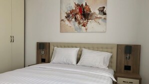 Une chambre à coucher avec un grand lit, deux tables de chevet avec des lampes, une tête de lit en bois et un tableau accroché au mur.