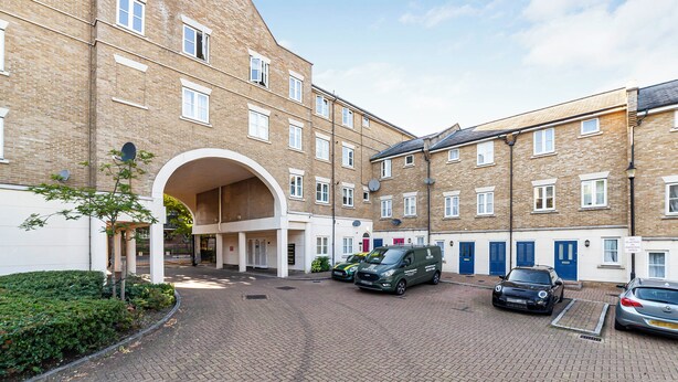 A multi-story building with a brick facade, a covered entrance, and several parked cars. - The Brixton Collection (London)