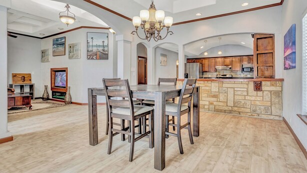 A spacious dining area with a wooden table and chairs, a chandelier, and a kitchen in the background. - The jewel of Mediterranean (San Antonio)