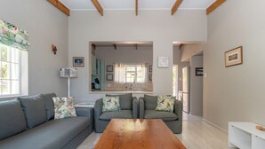 Sala de estar con una mesa de centro de madera, sofás grises y una cocina visible a través de un arco.