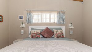 Un dormitorio con una cama grande, almohadones estampados con motivos florales, una ventana con cortinas, lámparas de noche y un cuadro enmarcado en la pared.