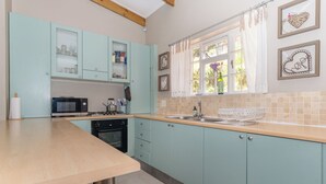 Una cocina con armarios verde azulado, encimera de madera, microondas, estufa y fregadero.