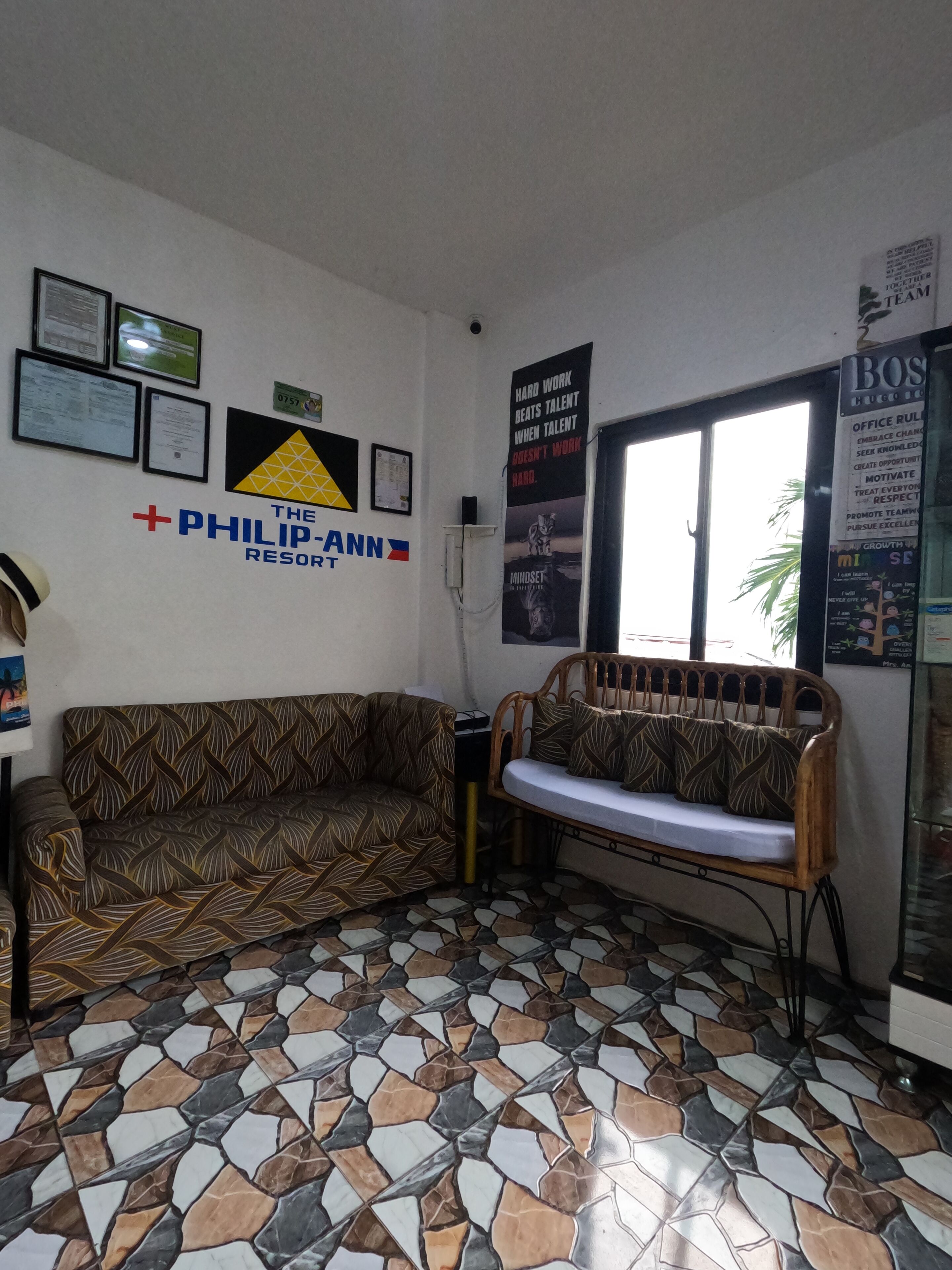Una habitación con sofás estampados, piso de baldosas y una pared decorada con varios carteles y un letrero de 'The Philip-Ann Resort'.