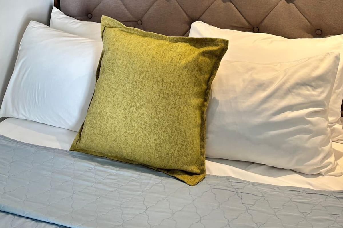 A bedroom with a tufted headboard, a round mirror with a circular frame, and a bed with white and green pillows.