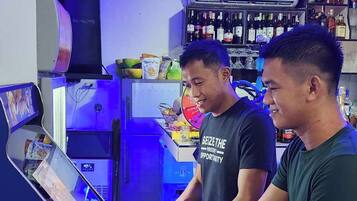 Un área de bar con mostrador, estantes llenos de botellas y dos personas de pie.