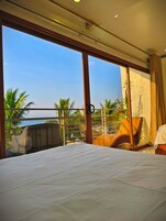 Habitación de hotel con un amplio ventanal que ofrece vistas a palmeras y al océano.