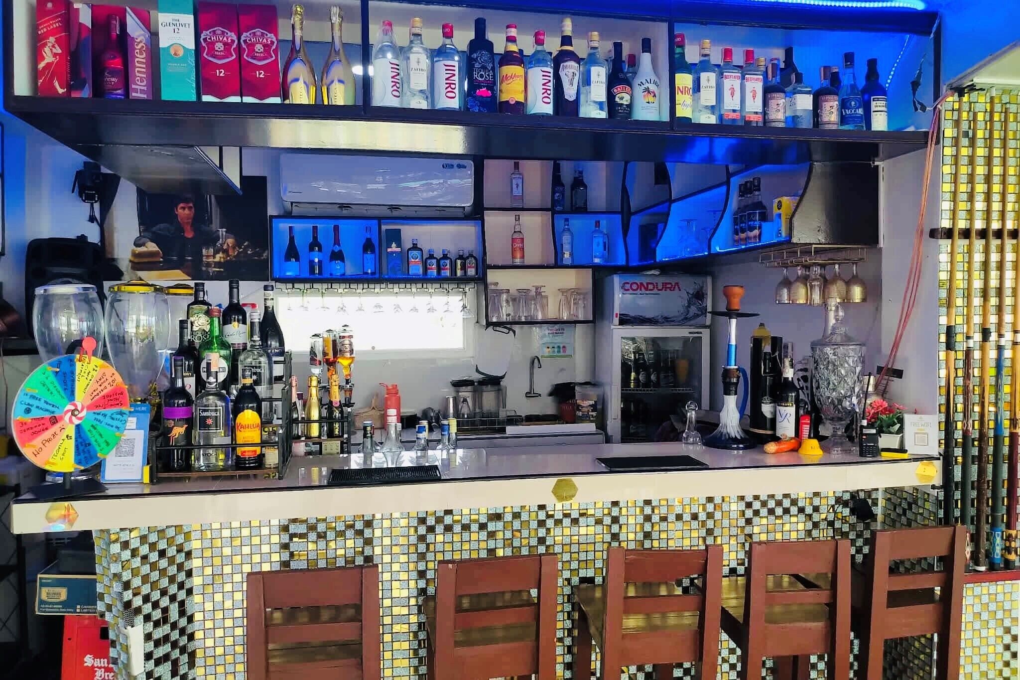A bar area with shelves of liquor bottles, a spinning wheel, and a tiled backsplash.