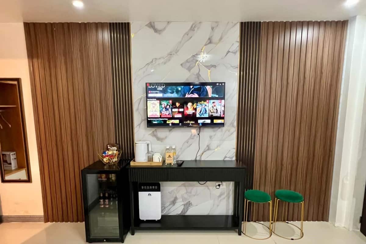 A modern living room with a marble wall, a mounted TV, a small black entertainment unit, and two green stools.