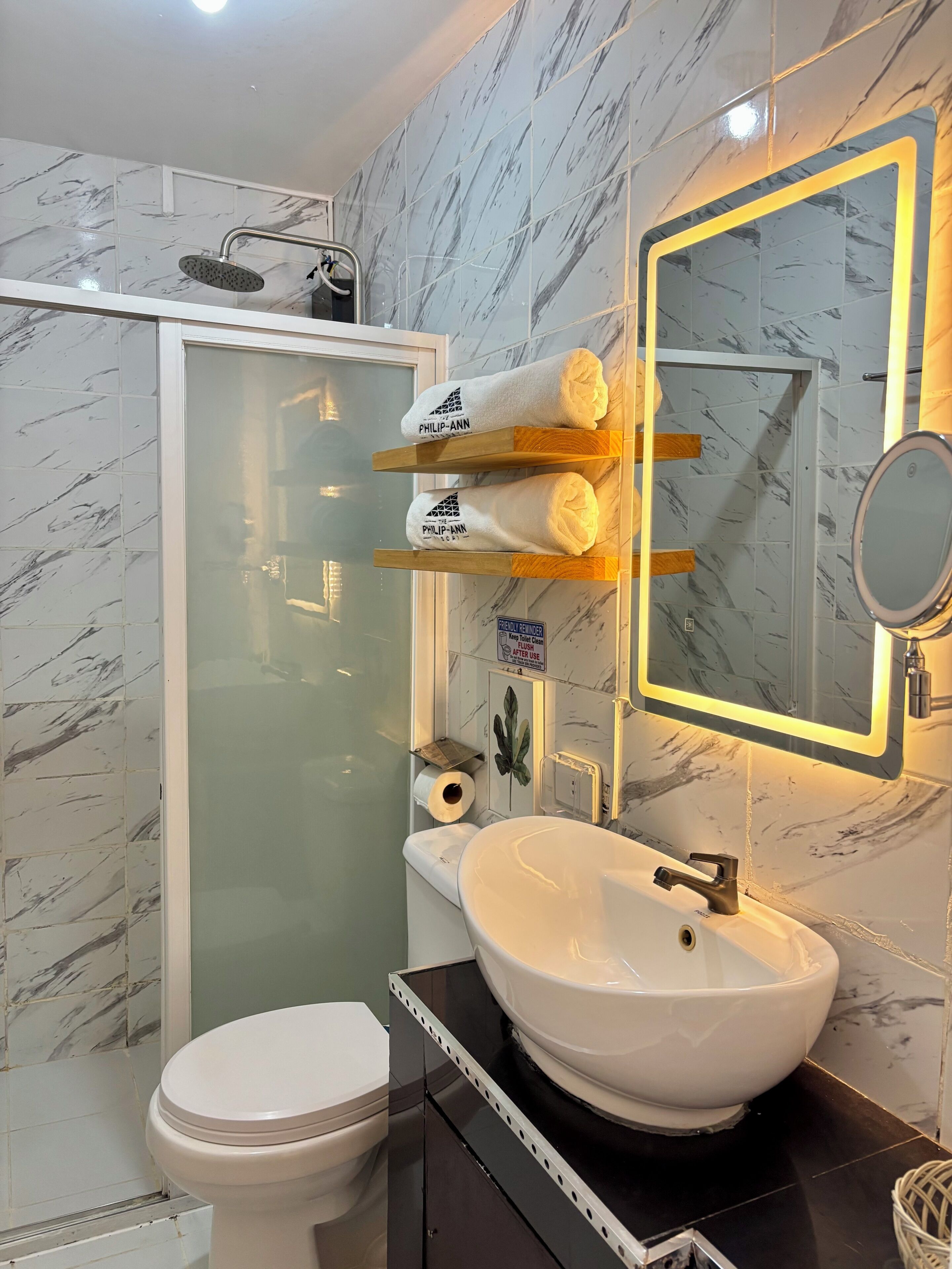 A bathroom with a glass-enclosed shower, a white toilet, a white sink with a mirror, and a towel rack with two towels.