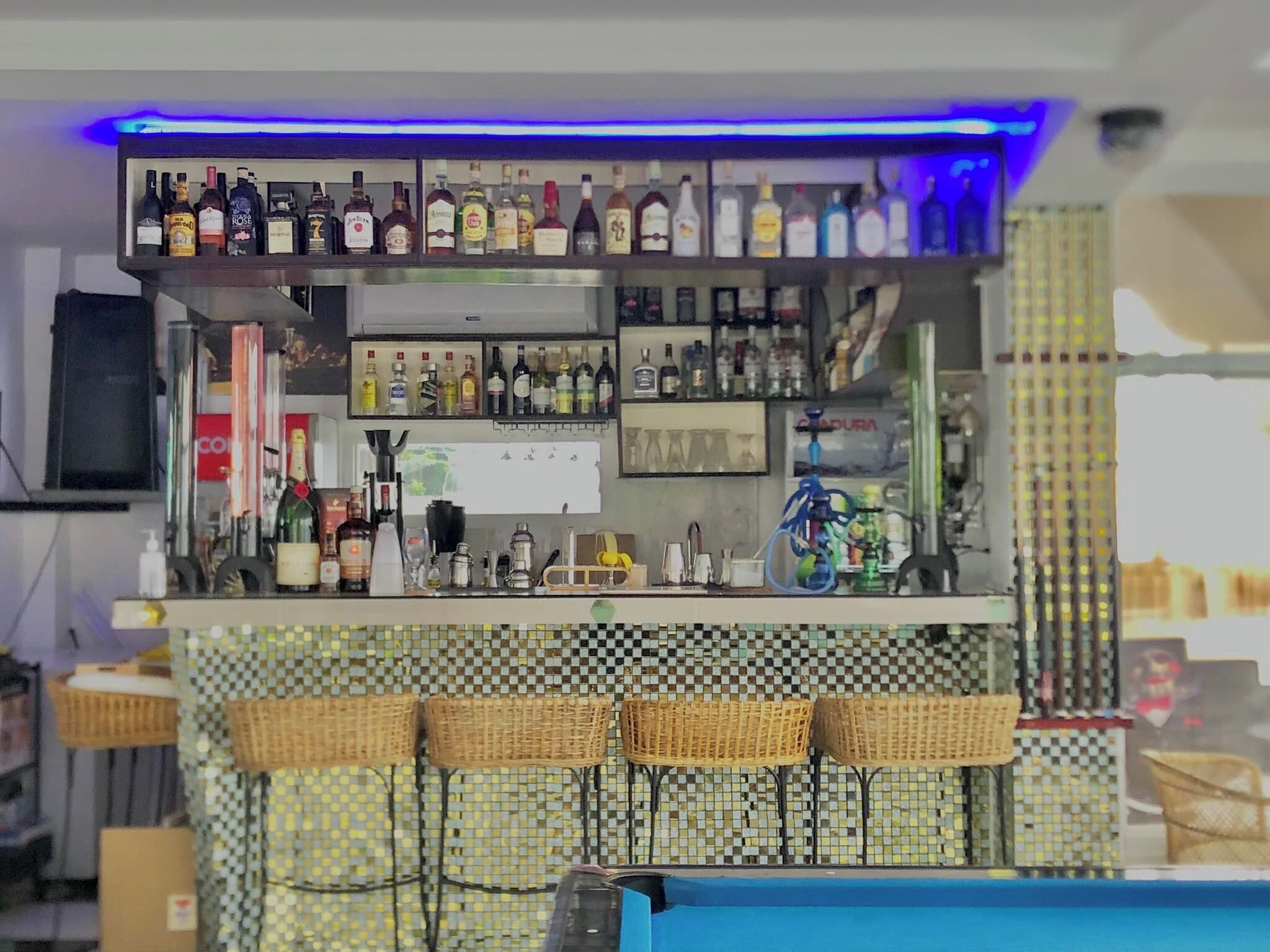 A bar area with shelves of liquor bottles, a hookah, and wicker bar stools.