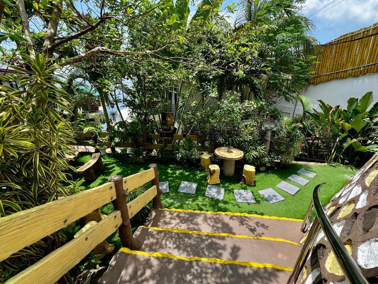 A wooden staircase leading to a garden area with a wooden bench, a round table, and a small statue.