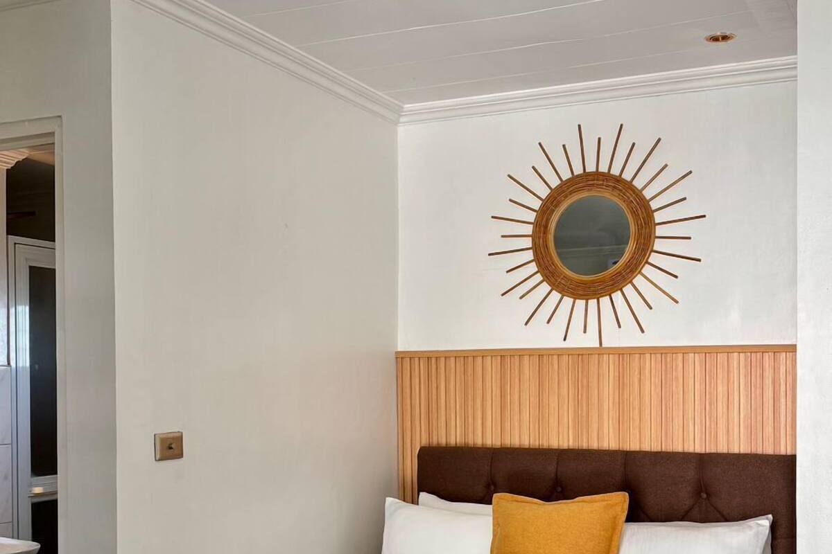 A bedroom with a bed, a headboard, a wall-mounted mirror, and a ceiling light.