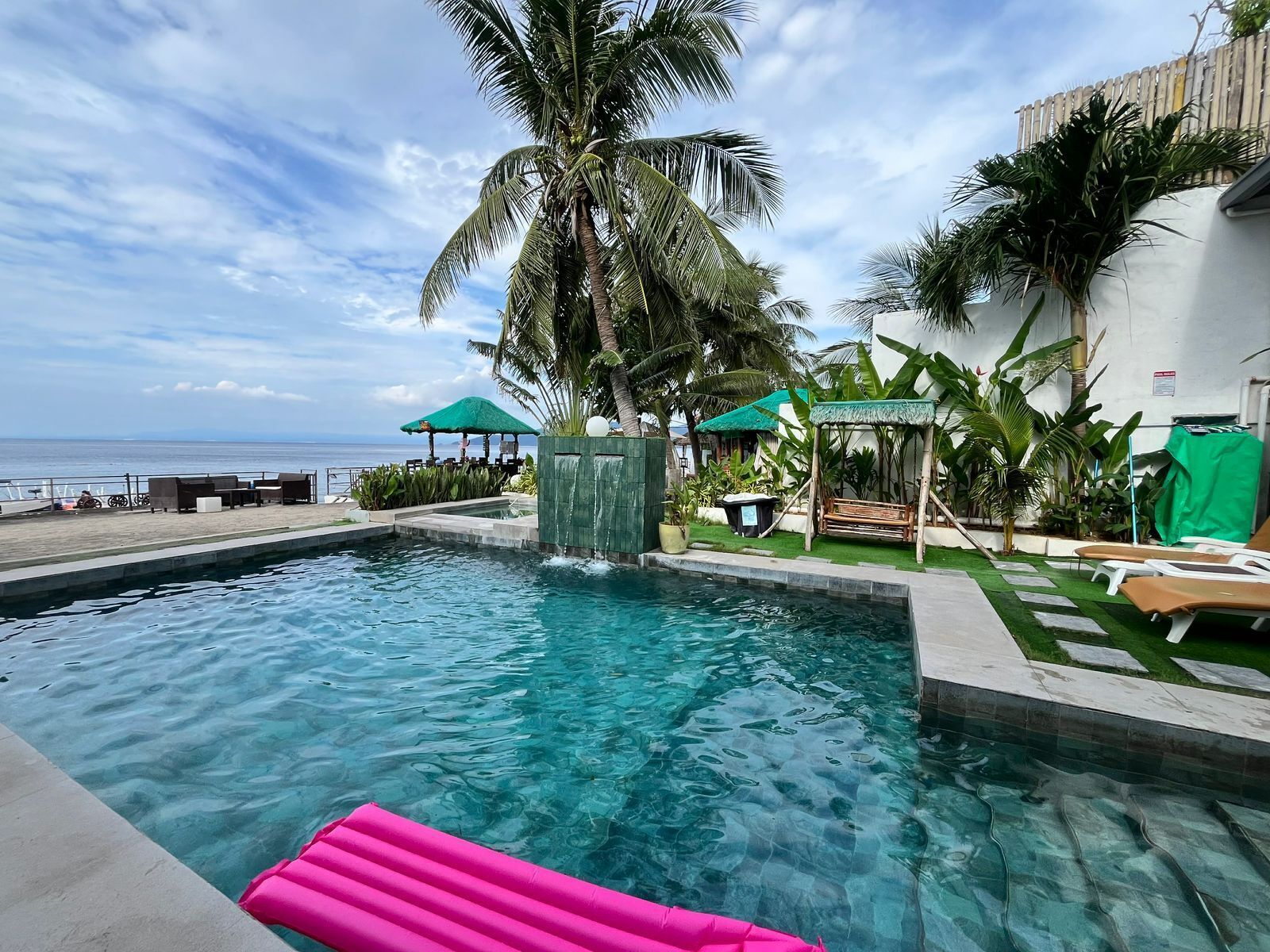Une piscine avec vue sur l’océan, entourée de palmiers et de chaises longues.