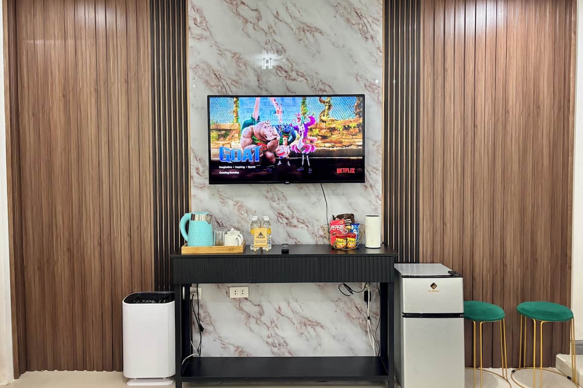 A modern living room with a flat-screen TV mounted on a marble wall, a black entertainment unit below, and a white mini-fridge to the right.