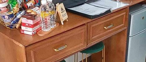 A wooden desk with a television, a small refrigerator, and various items on the desk.