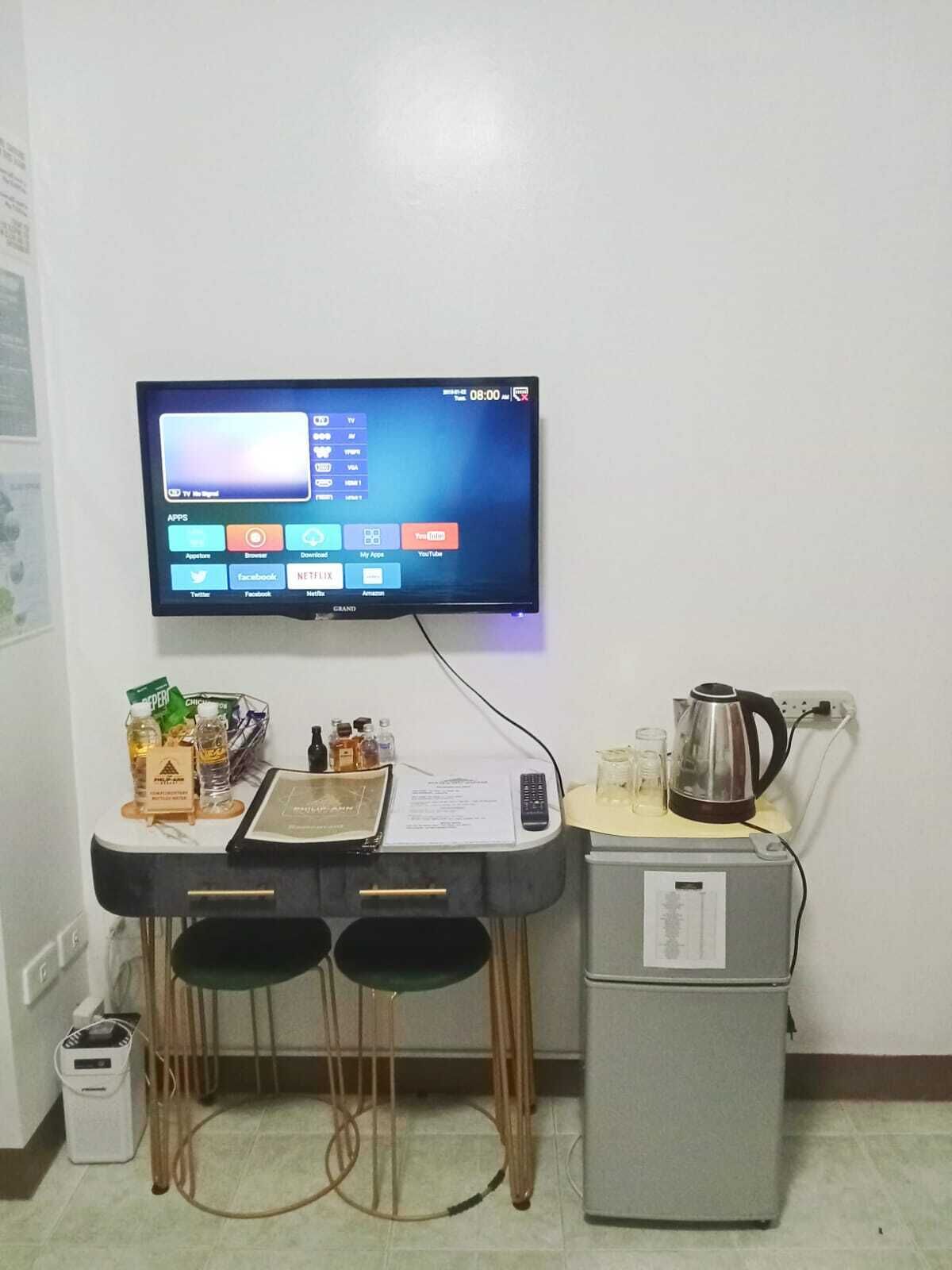 Een kleine kitchenette met een televisie aan de muur, waarop een beginscherm te zien is.