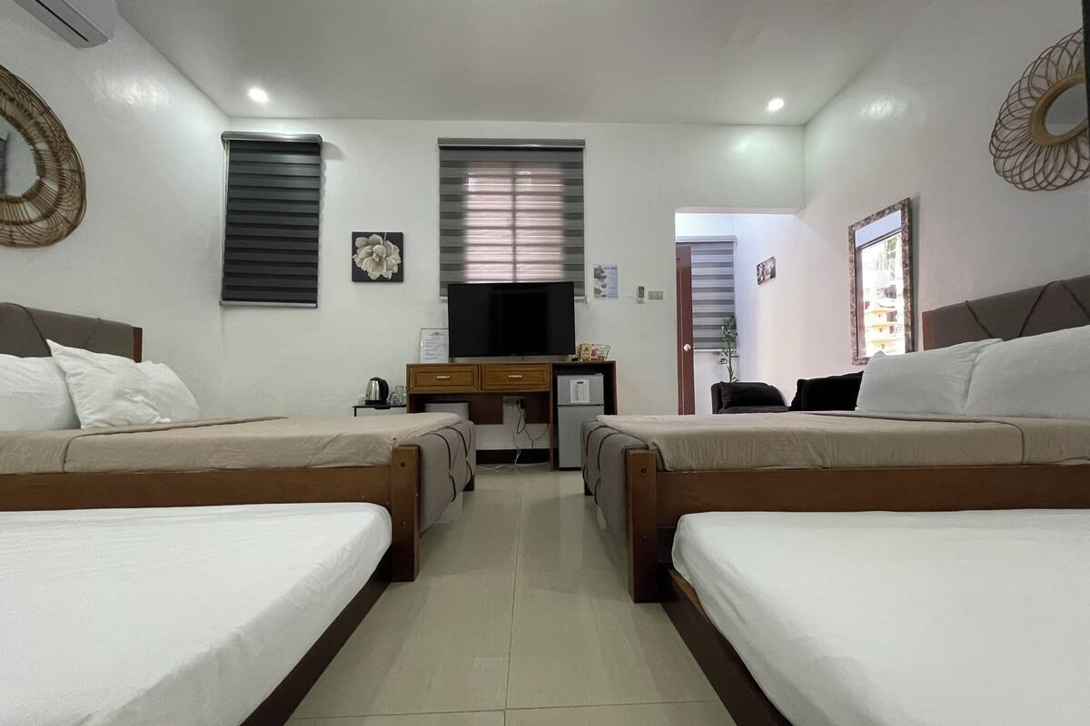 A hotel room with two single beds, a desk with a chair, a television, and a window with blinds.