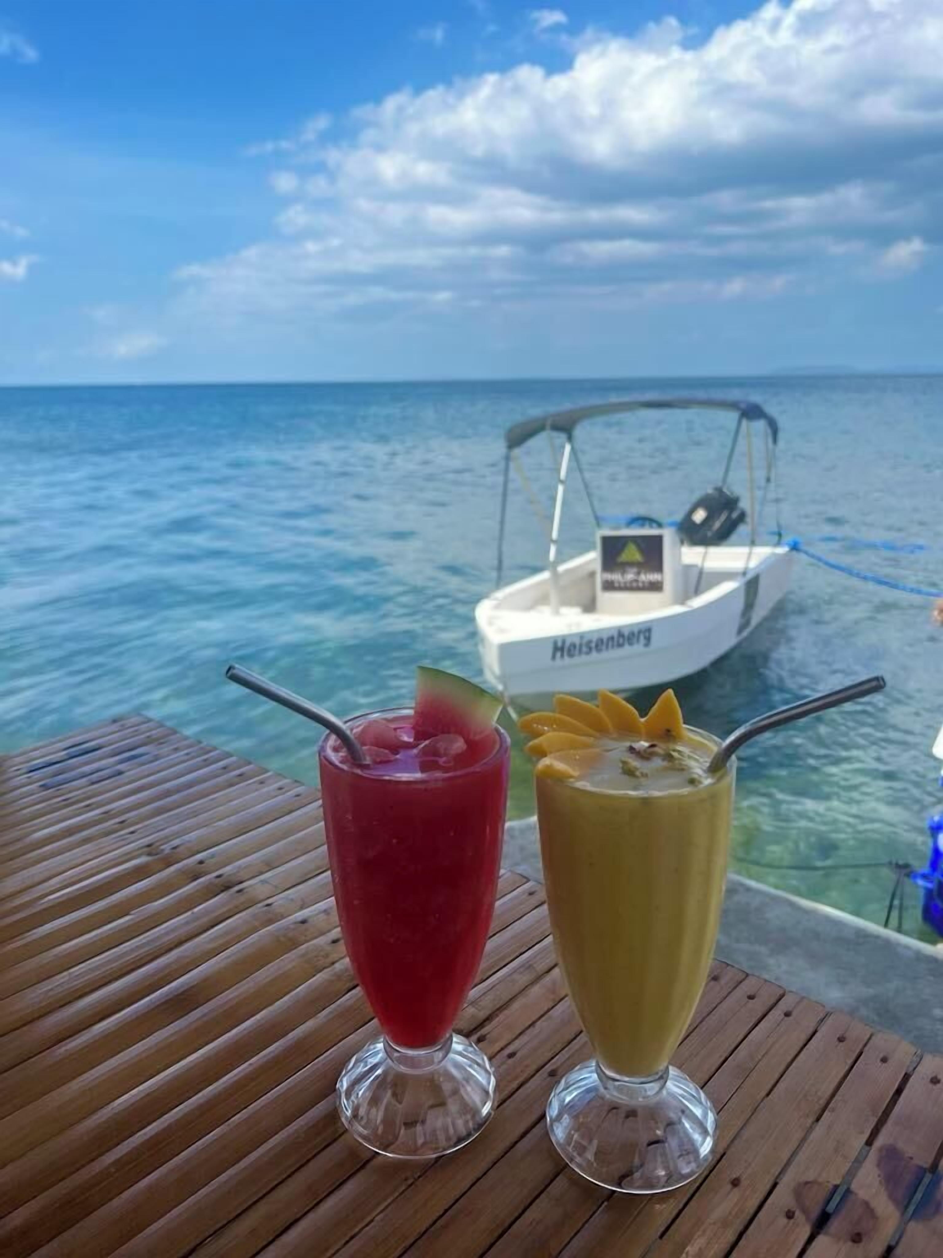 Two drinks on a wooden table with a boat in the background.