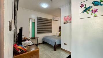 Un dormitorio pequeño con cama, escritorio, silla y ventana con persianas.