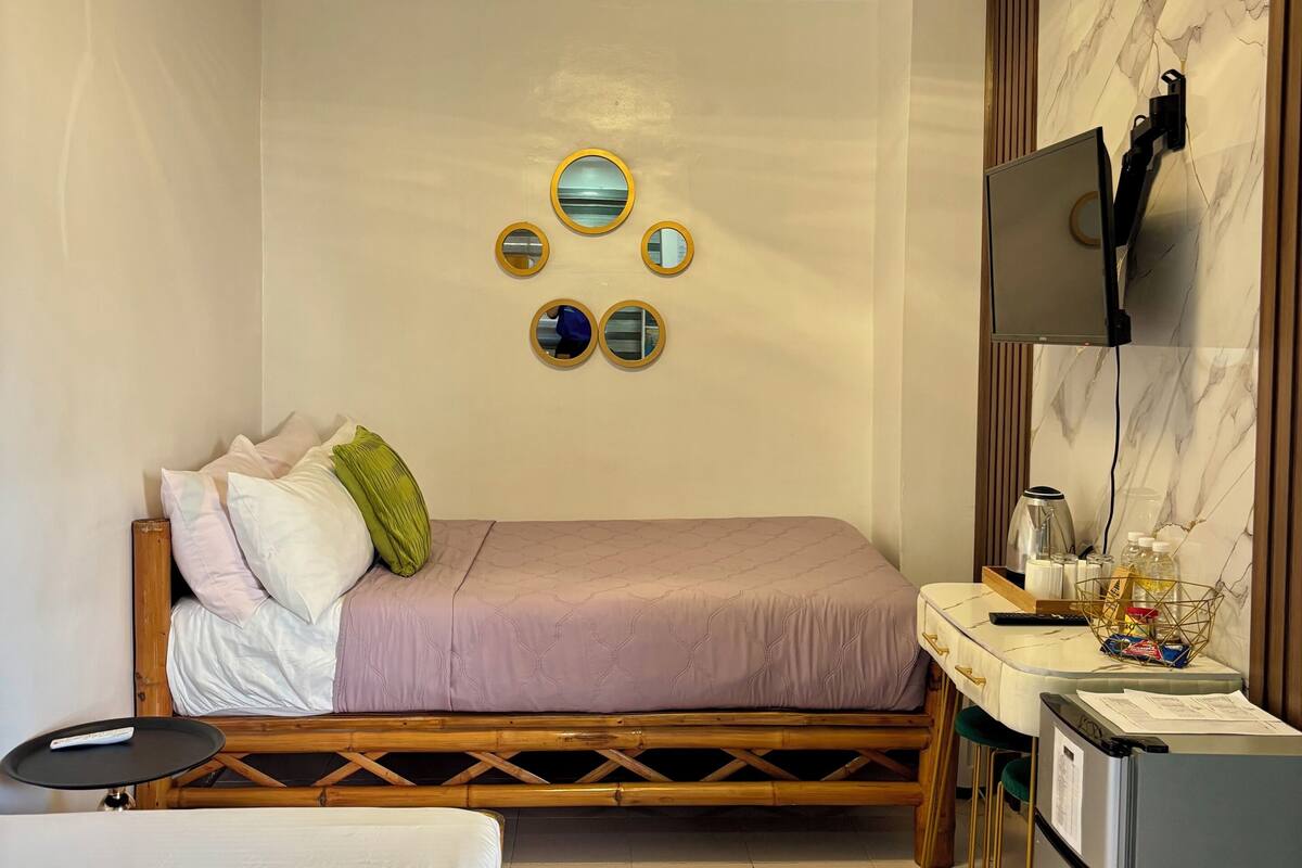 A hotel room with a bed, a desk, a refrigerator, and a wall-mounted TV.
