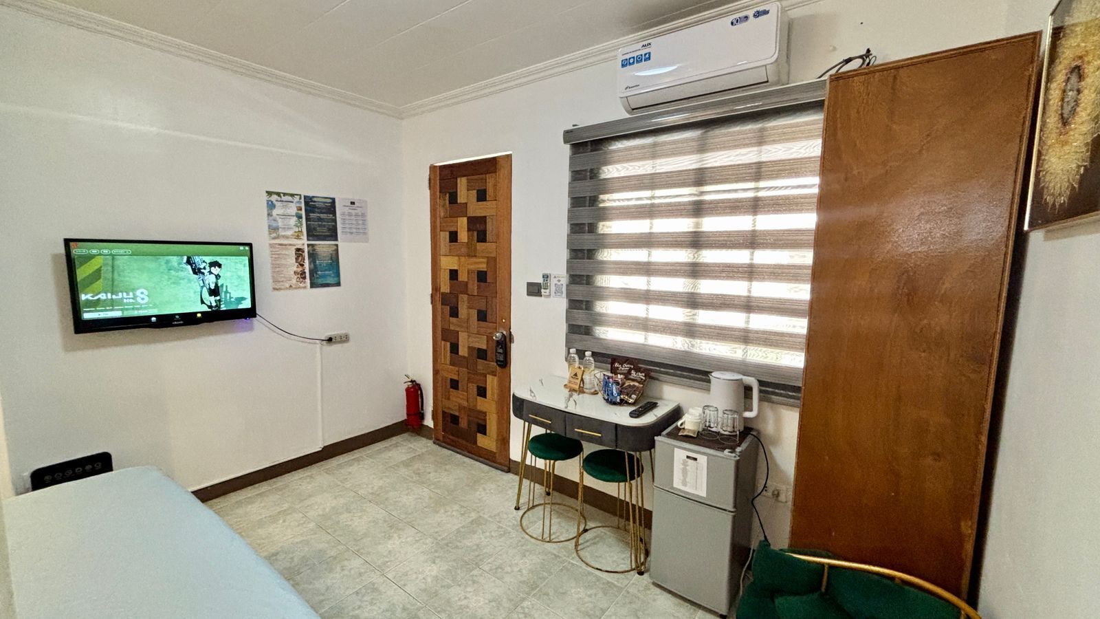 A small kitchenette with a TV, a wooden door, a window with blinds, and a fire extinguisher.