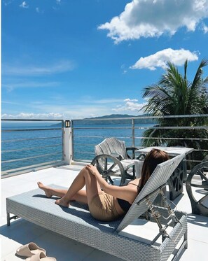 A woman relaxing on a lounge chair by a pool with a view of the sea and mountains. - The Philip Ann Resort (Mabini)