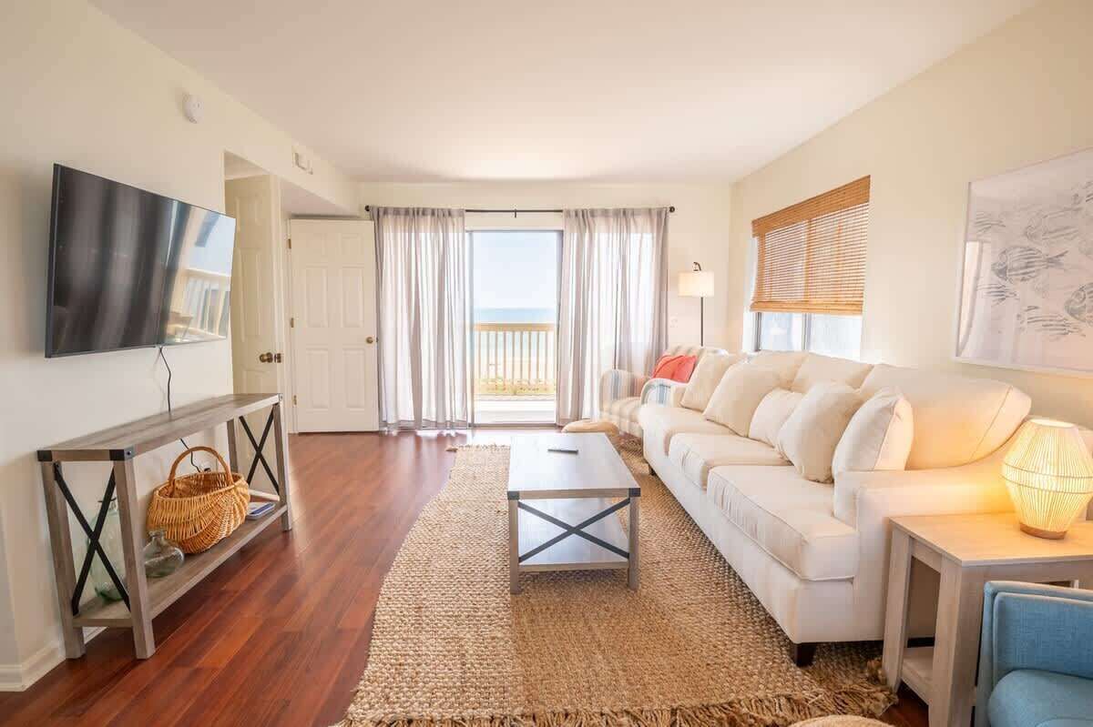Una sala de estar con sofá, mesa de centro, televisor y un gran ventanal con cortinas.
