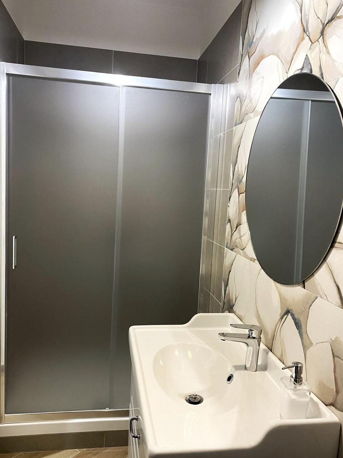 Un baño moderno con cabina de ducha, un espejo grande y un lavamanos blanco.