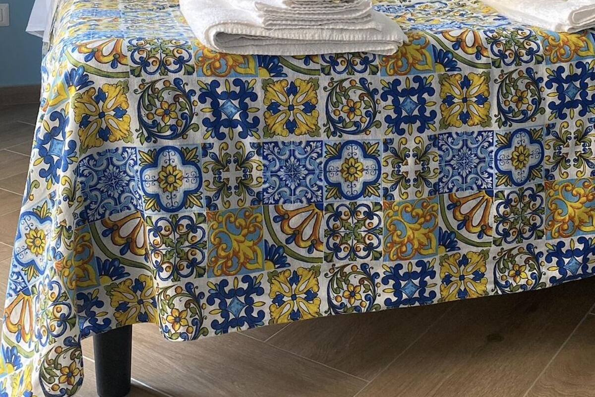 Una cama bien hecha con una colcha estampada, dos almohadas y una toalla doblada sobre un piso de madera.