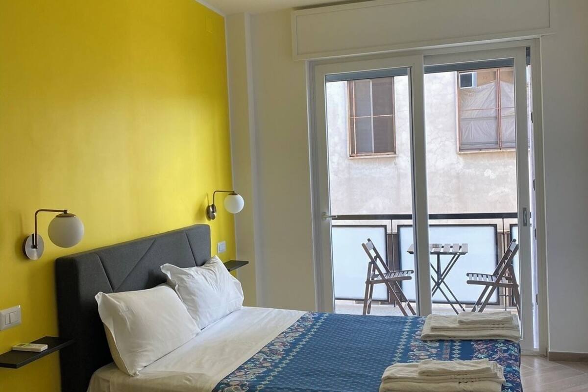 Un dormitorio con cama, lámparas de noche, una ventana y un balcón con sillas.