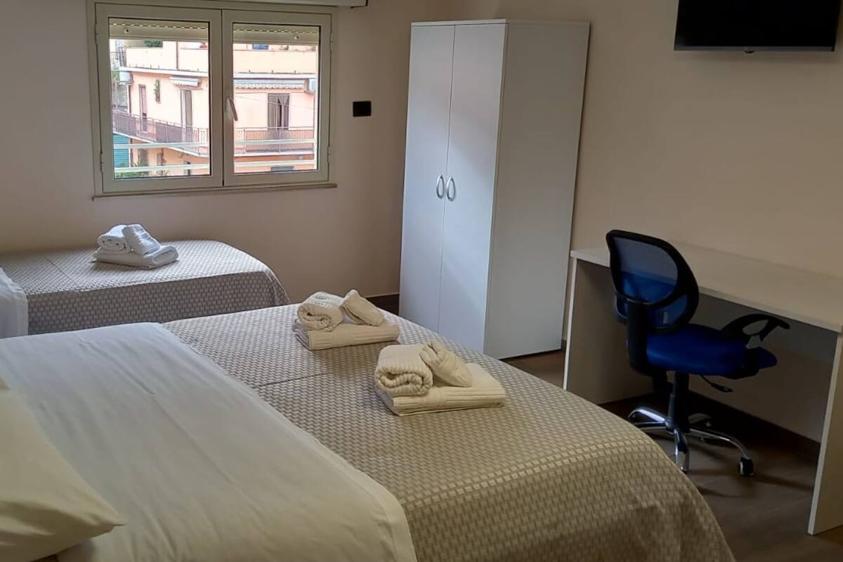 A hotel room with two beds, a desk, a chair, and a wardrobe.