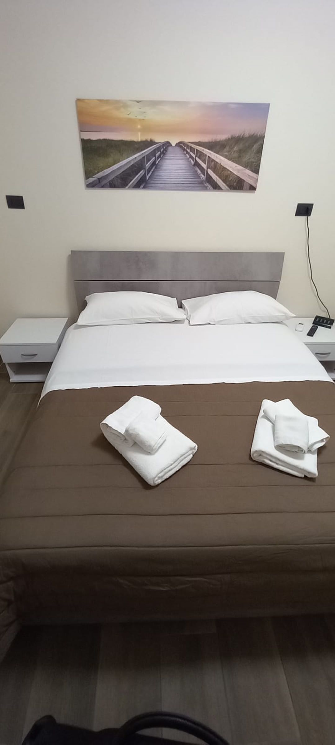 Une chambre d’hôtel avec un lit, du linge de lit blanc, un matelas marron et deux serviettes pliées posées sur le lit.