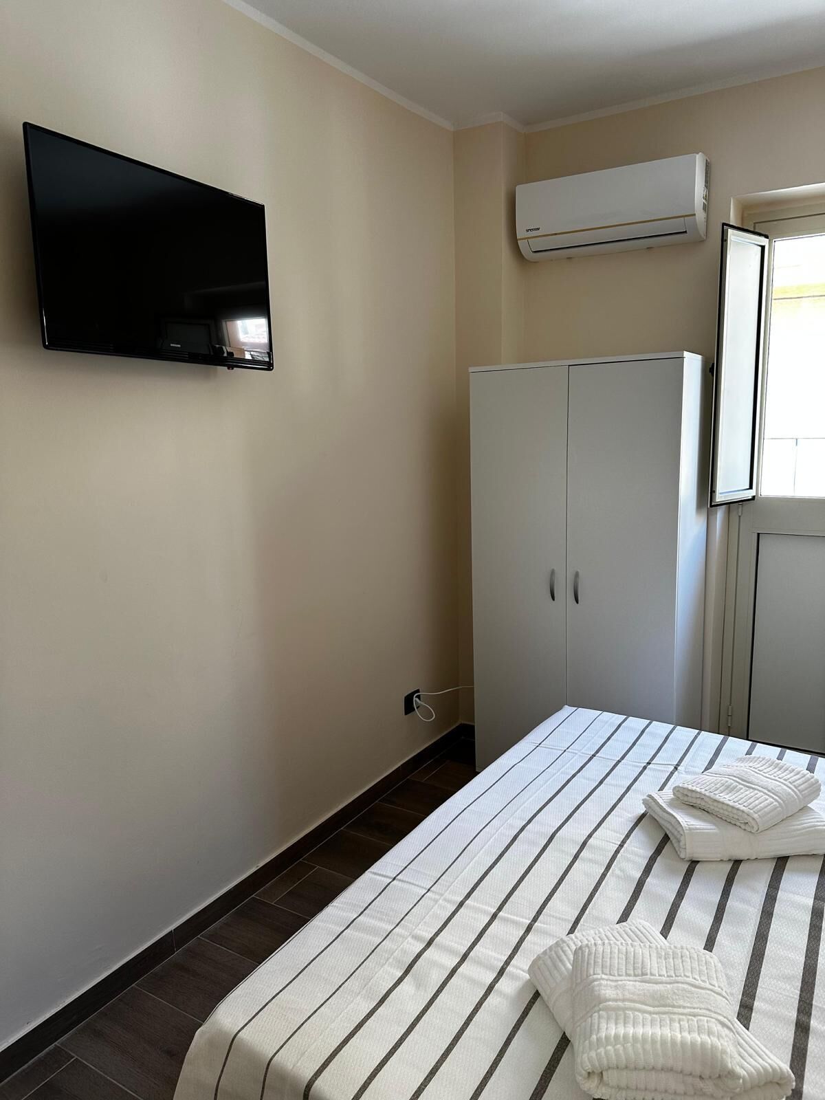 Una habitación de hotel con cama, televisor, aire acondicionado y armario.