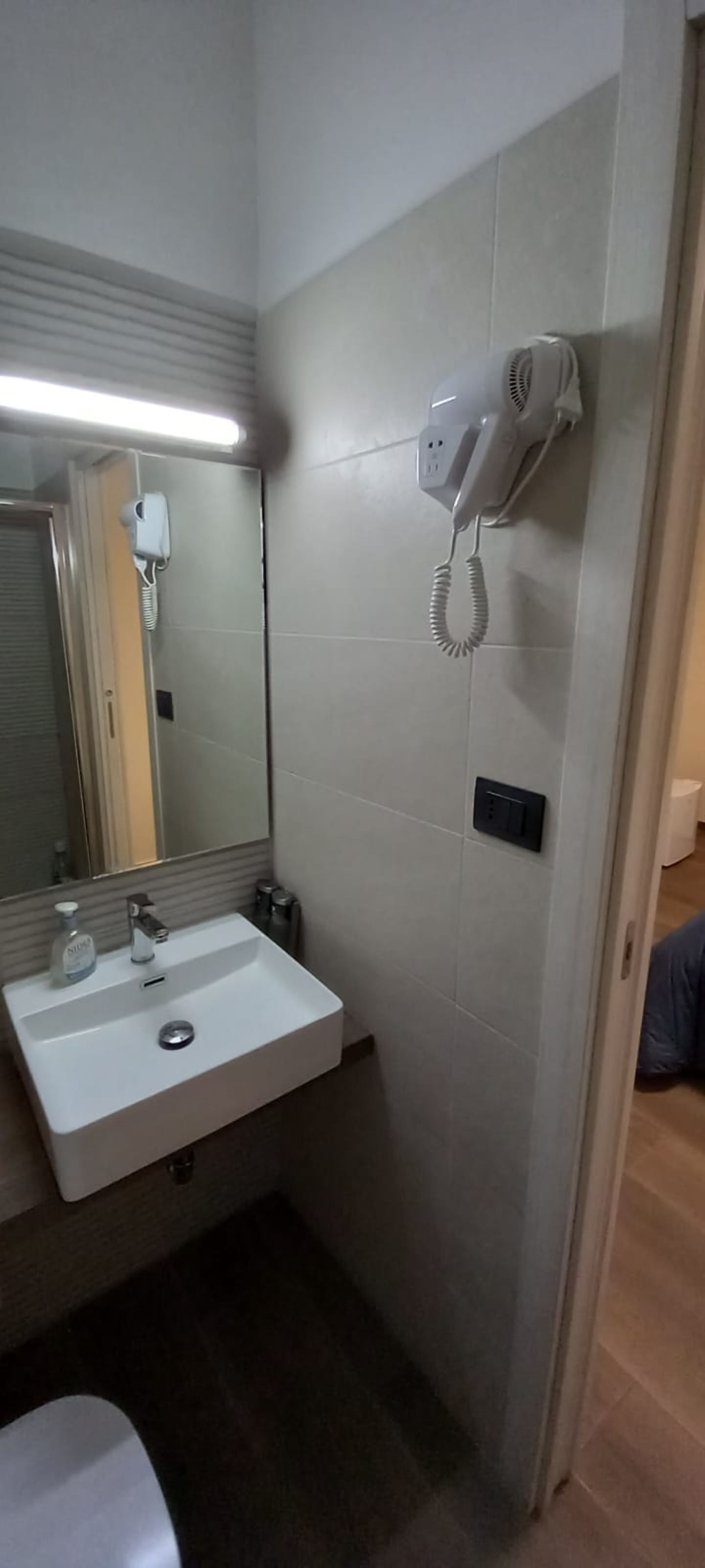 Casa de banho com uma pia branca, um espelho, um secador de cabelo e um interruptor de luz na parede.