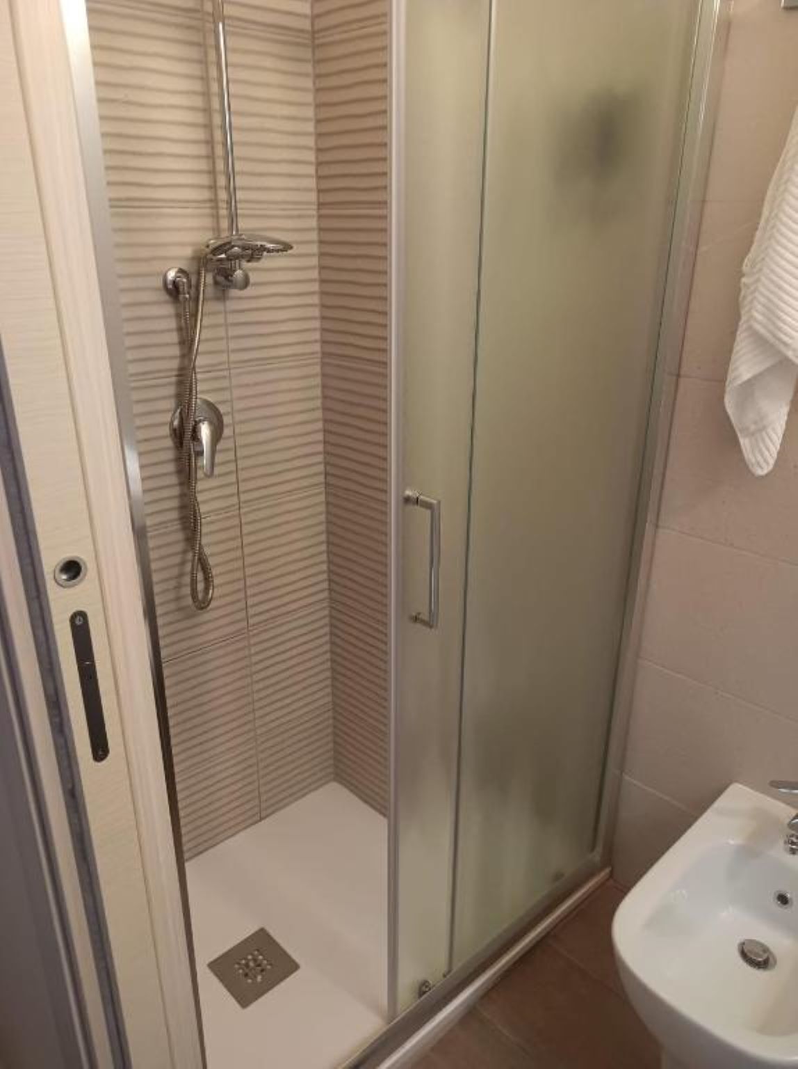 A glass-enclosed shower with a handheld showerhead and a wall-mounted faucet.