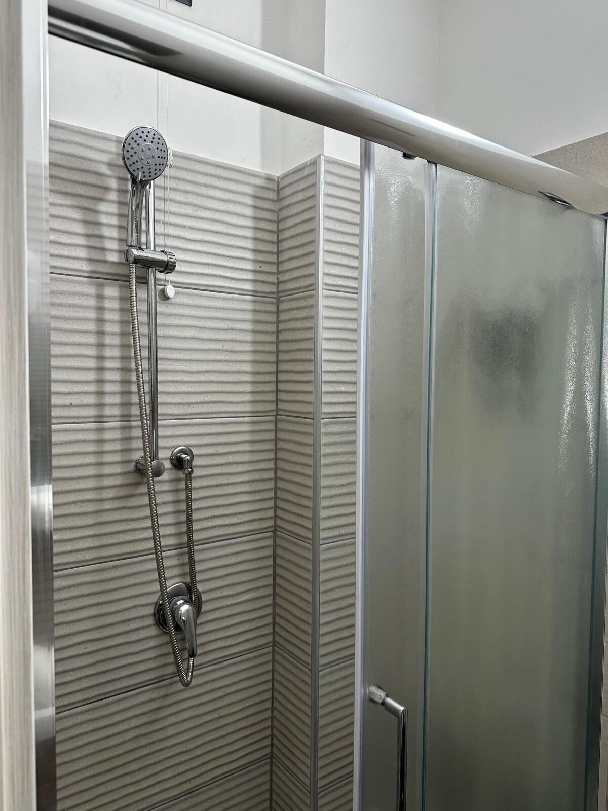 A corner shower with a handheld showerhead and a handheld shower attachment.