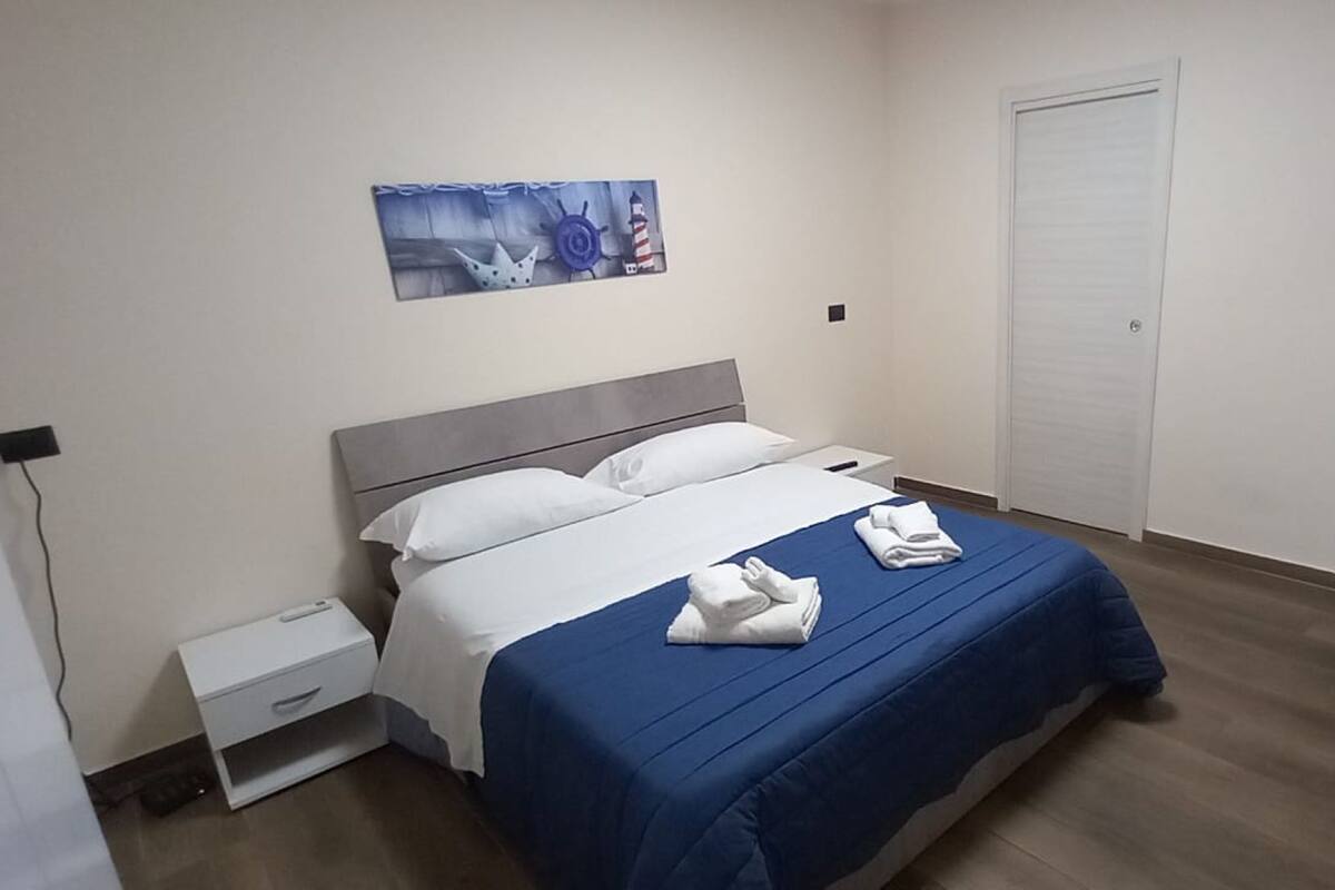 A bedroom with a bed, a nightstand, a wall-mounted painting, and a door.