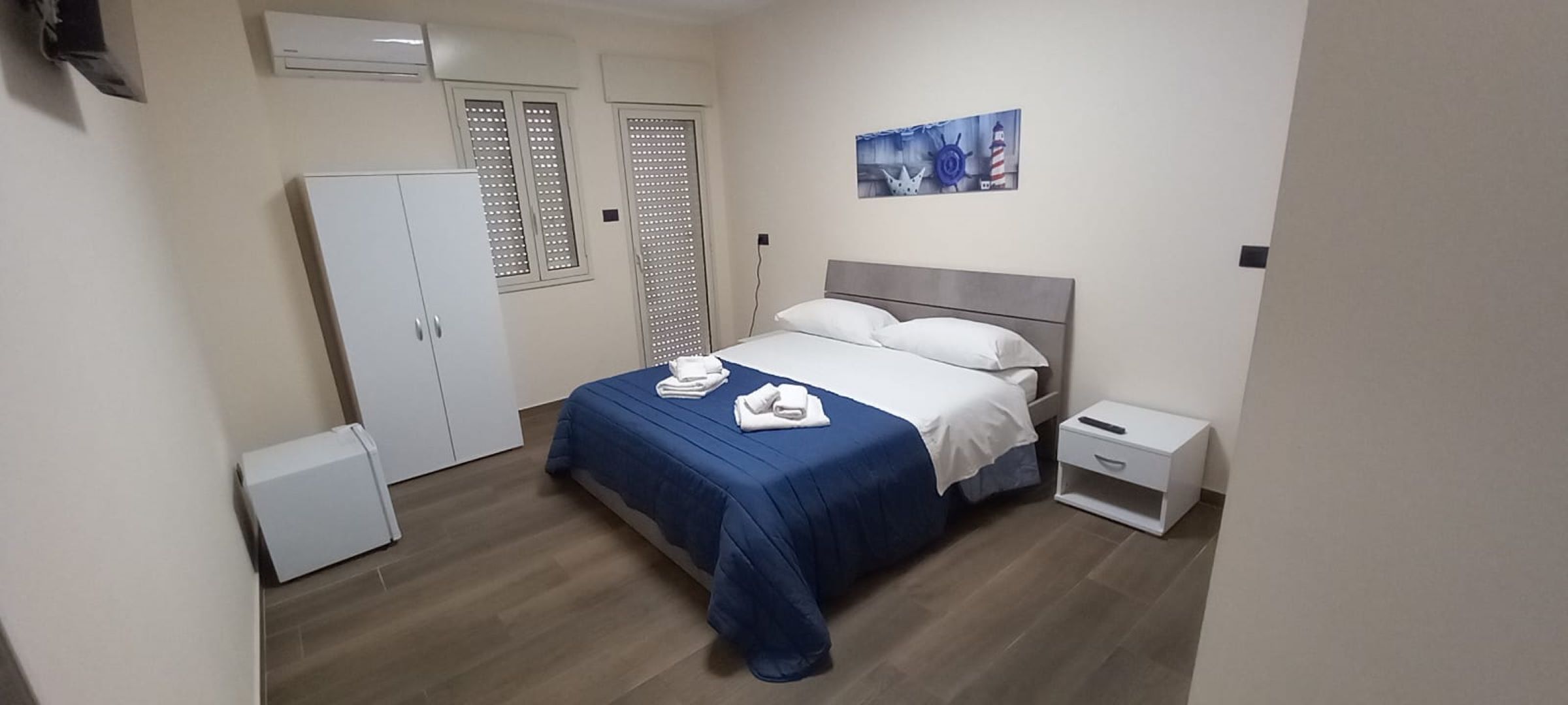 A bedroom with a bed, a wardrobe, a nightstand, and a wall-mounted air conditioner.