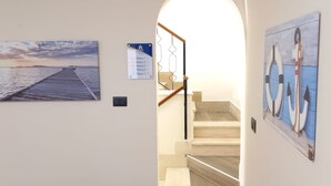 A hallway with a wooden staircase, a view of the sea, and a sign indicating room numbers. - B&B Omnia Scilla (Scilla)