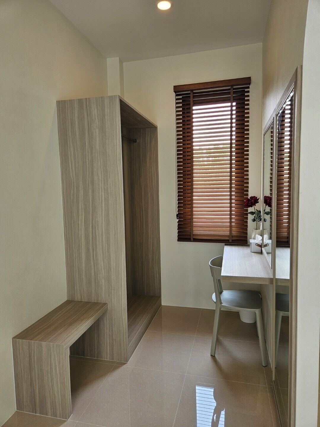 A bathroom with a wooden vanity, a bench, a mirror, and a window with blinds.
