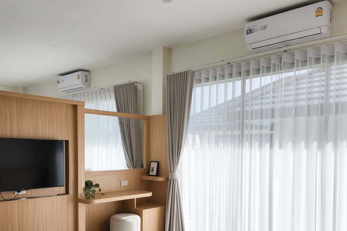 Ein modernes Hotelzimmer mit einem großen Bett, einem flachbildfernseher an der Wand, einer Holztischlerei mit Spiegel und einer Klimaanlage über dem Fenster.