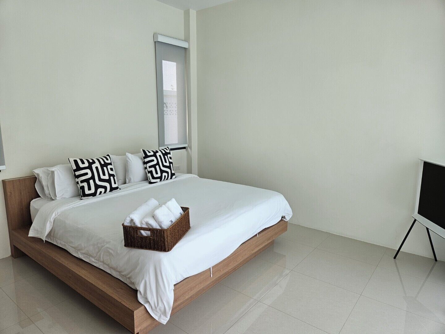 A modern bedroom with a wooden bed, white bedding, and a wicker basket with towels.