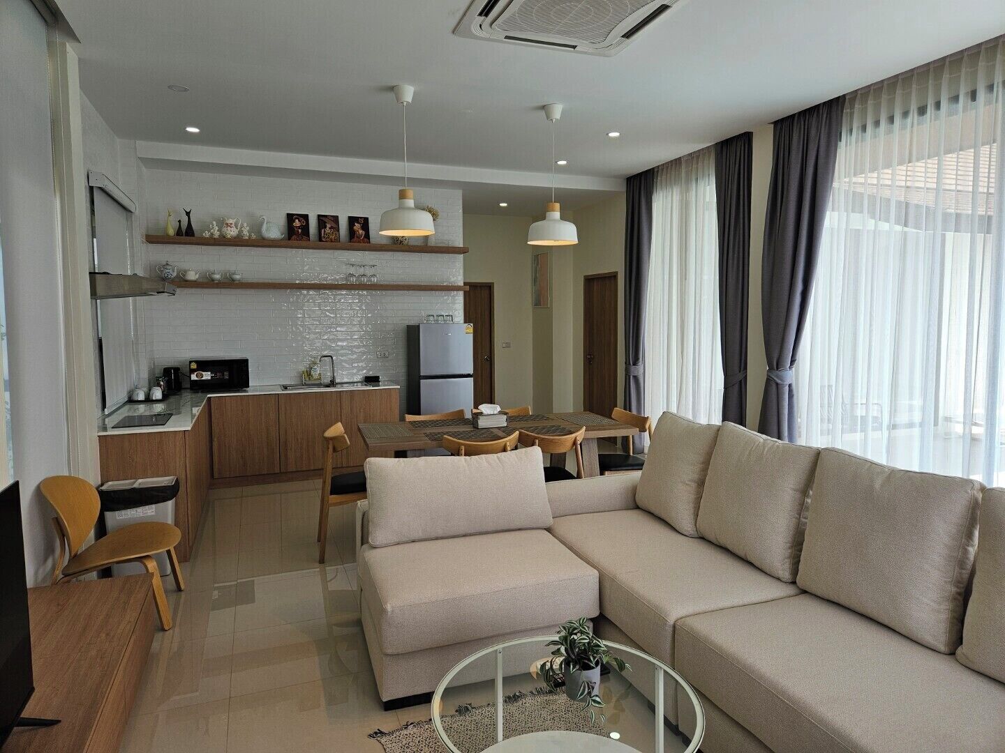 A modern living room with a beige sofa, a glass coffee table, and a dining area with a table and chairs.