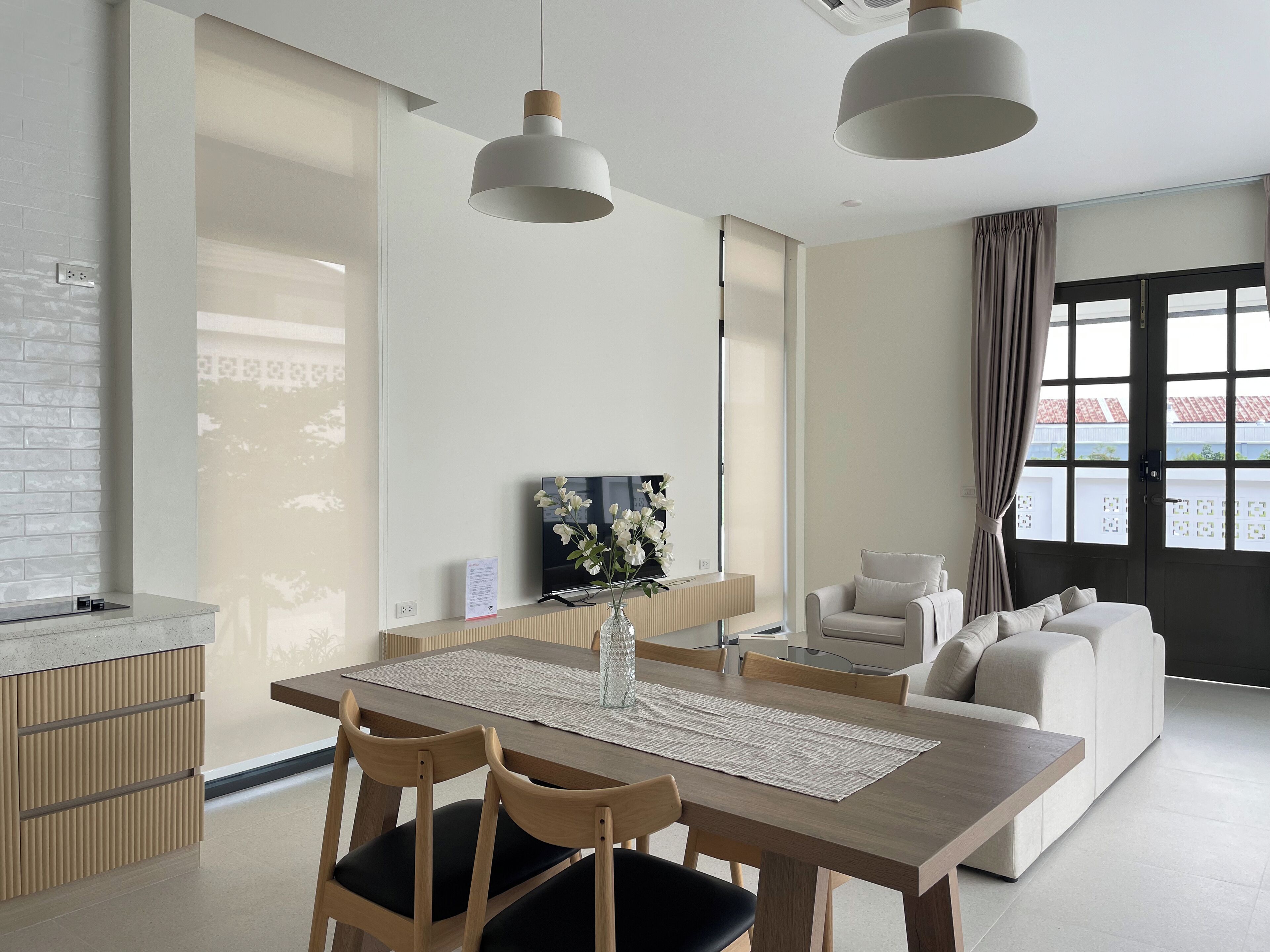 A modern living room with a dining area, featuring a wooden table, chairs, a sofa, and a TV.